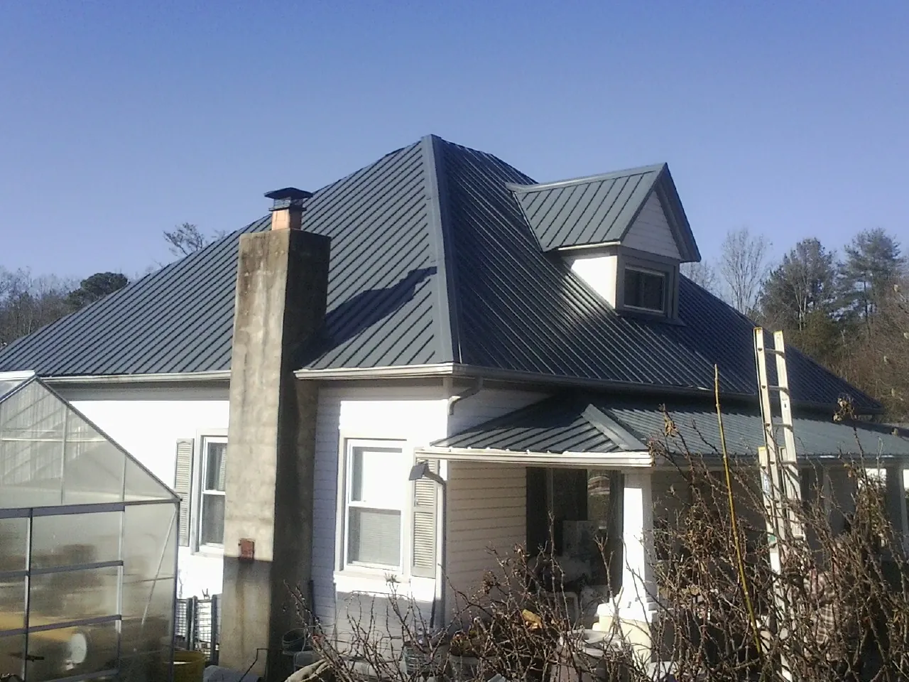 Dark blue standing seam metal roof on a white farmhouse with dormer — Slate & Tile Roof Repair by Roofing Brothers in Mc Intire