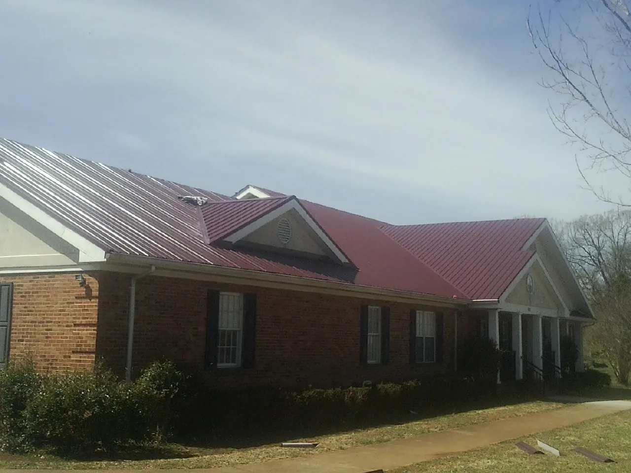 Red metal roof with gabled entries on a long brick building, from a Hail Damage Roof Repair job in Mc Intire