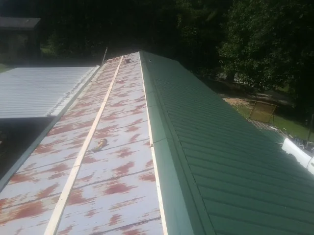 Old rusted panels beside newly installed green metal roofing — Wind Damage Roof Repair by Roofing Brothers in Mc Intire