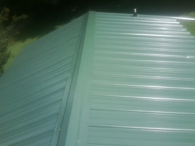 New green metal panels meeting at the ridge of a roof — Flat Roof Repair work by our crew in Mc Intire