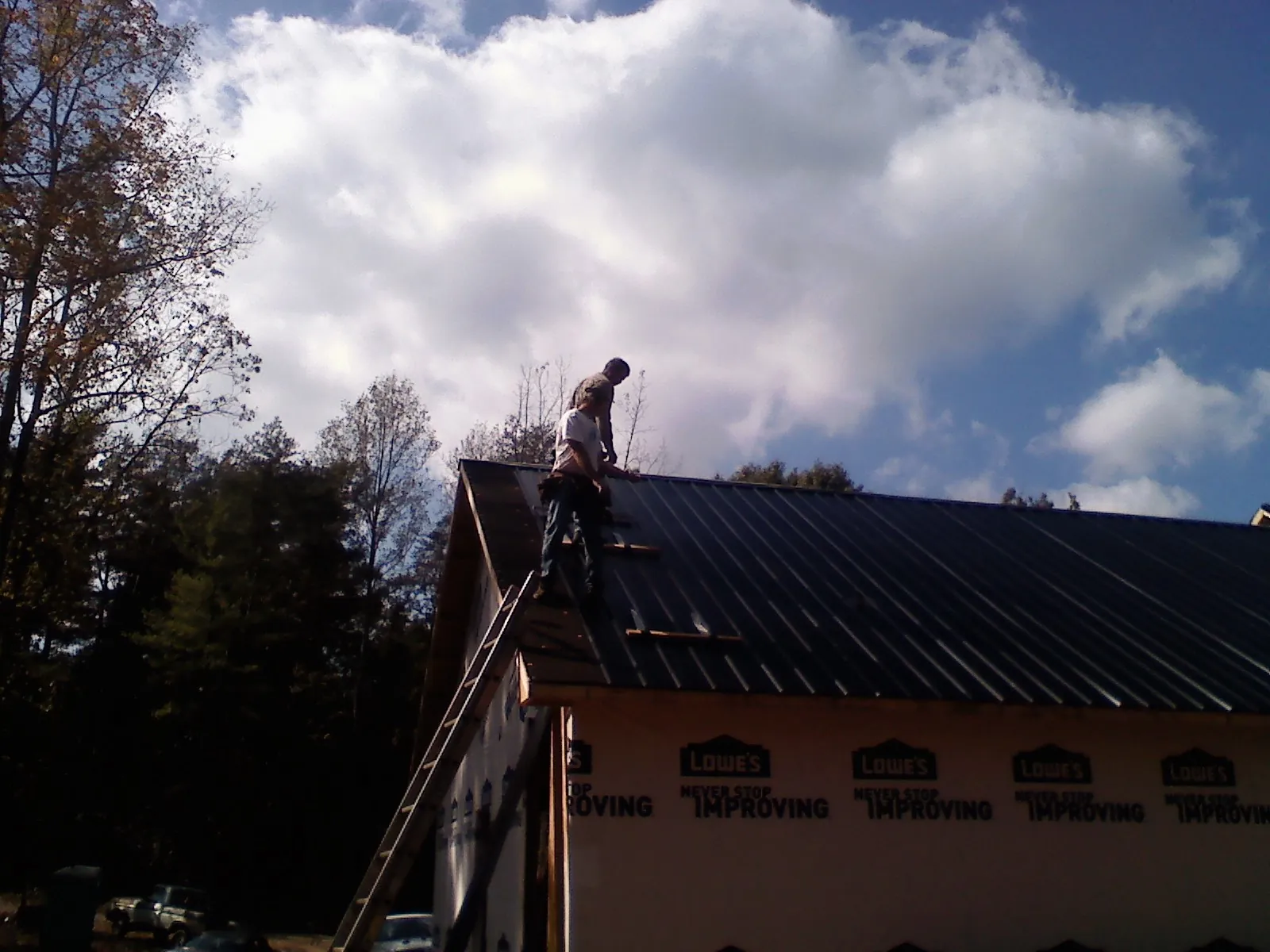 Roofer fastening dark metal panels high against a cloudy sky, from a Roof Inspection job in Mc Intire
