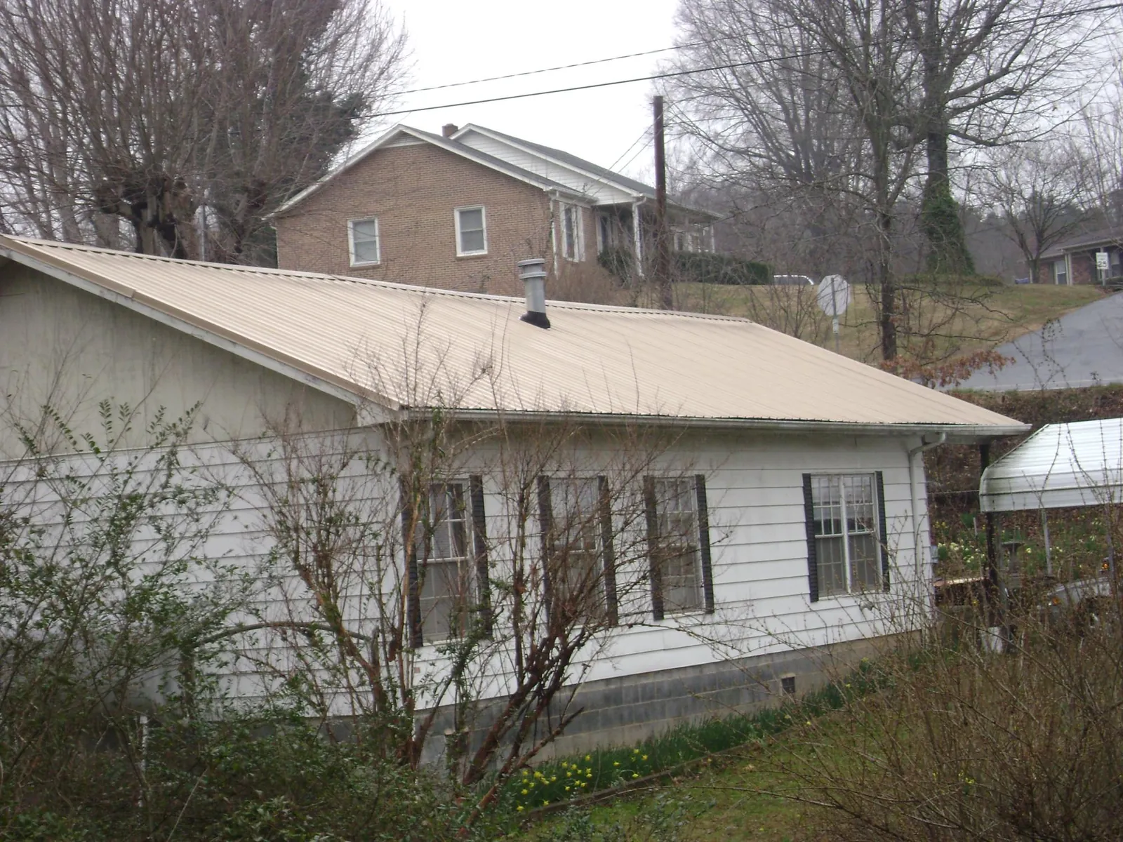 Tan metal roof on a white sided house set into a hillside — Commercial Roofing by Roofing Brothers in Mc Intire